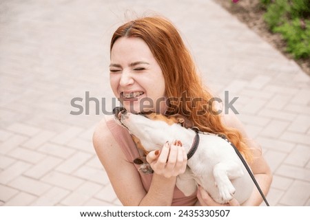 Dog jack russell terrier licks the owner in the face outdoors. Girl with braces on her teeth. 