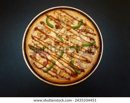A freshly-baked pizza with onions, capsicum slice, bell peppers, chicken and a drizzle of BBQ sauce on a wooden board and pizza tray.
