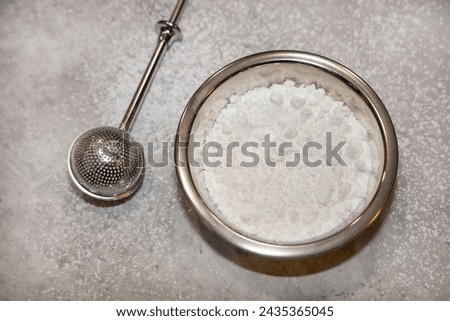 View of a small bowl of powdered sugar and a stainless steel sugar duster on the side.
