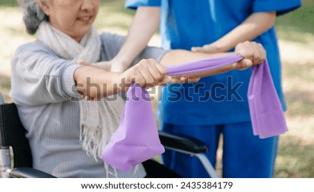 Asian physiotherapist helping elderly woman patient stretching arm during exercise correct with dumbbell in hand during training hand with patient Back problems in garden. Nursing home hospital 