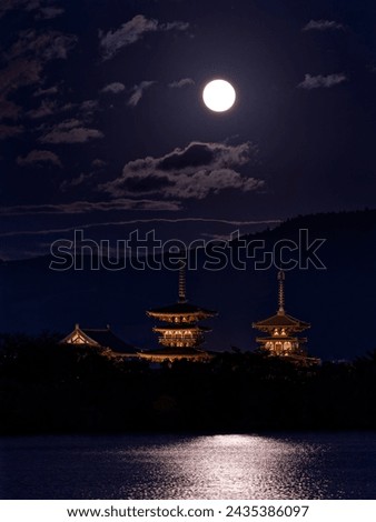 The full moon reflects light on the pond and the illuminated three-storied pagoda of Yakushiji Temple Royalty-Free Stock Photo #2435386097