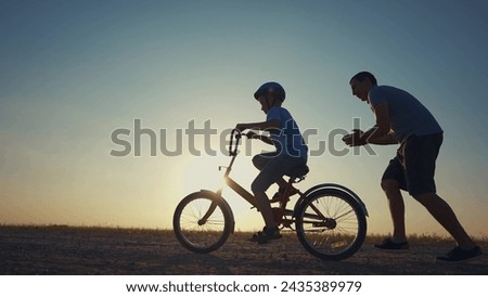 family play in the park. father teaching son to ride a bike. happy family kid dream concept. son learn to ride bike silhouette. father supporting sunset child son riding bike summer in the park