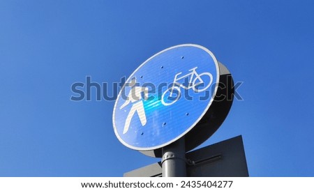 Be aware of pedestrians crossing and bike lines ahead with blue and white round traffic signs on a tall pole with a blue sky background and copy space. Closeup bottom side view. Traffic sign concept.