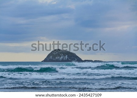 Sunset over Muriwai beach. Angry waves crashing onto the empty beach. Auckland, New Zealand. Royalty-Free Stock Photo #2435427109