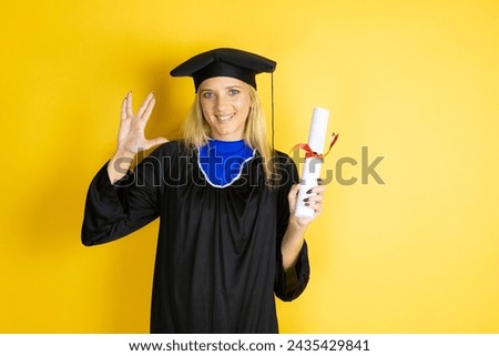 Beautiful blonde young woman wearing graduation cap and ceremony robe doing star trek freak symbol