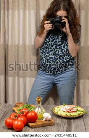 A food photographer taking a picture of arugula salad with cucumber and radish food on her digital camera. Young female photographer looking through camera lenses.
