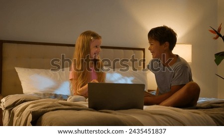 Laughing Caucasian happy children brother sister kids girl boy looking laptop screen in bedroom on bed evening watching cartoon video online using computer application enjoy watch funny show program