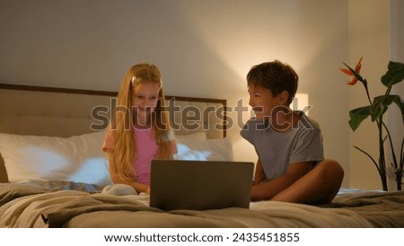 Laughing Caucasian happy children brother sister kids girl boy looking laptop screen in bedroom on bed evening watching cartoon video online using computer application enjoy watch funny show program