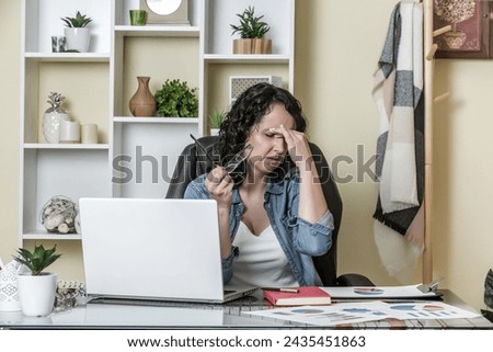 Exhausted adult woman with closed eyes taking off glasses and rubbing nose bridge while working on remote project in cozy workplace at home Royalty-Free Stock Photo #2435451863
