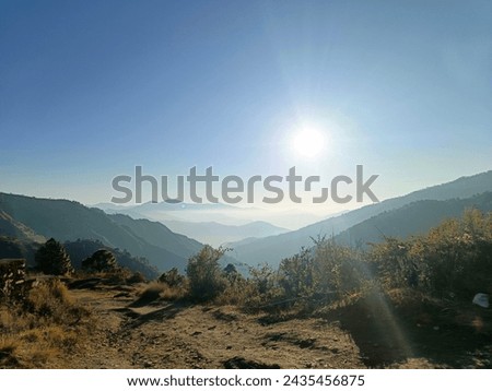 A beautiful shot of the majestic mountains, layered in the soft morning sunlight, with a clear expanse of sky and a winter fog that blankets the valleys of Uttarakhand.