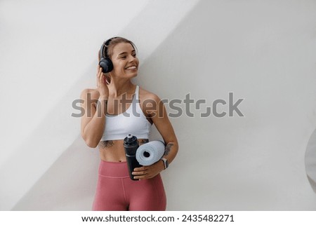 Young female runner is having break and listening to music in headphones during the run in city