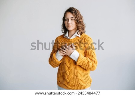 Grateful Young Woman: Expressing Happiness and Thankfulness - Hands on Chest, Mental Balance - Kindness, Love, and Gratitude - Isolated Portrait on White Background - Conceptual Image of Emotional Wel Royalty-Free Stock Photo #2435484477