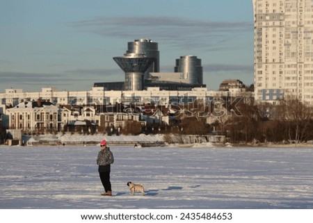 Woman with Pug in the snow. dog plays and runs. Snow on a snowy river. Embankment in winter. Sunny winter day. Blue sky.