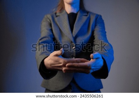 A business woman holds her hands outstretched forward, palms facing each other. No face. Blue color correction.