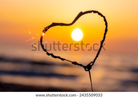 Heart-shaped sparkler burning against background of sea and rising sun at dawn. Bengal fire in shape of heart sparkling at sunrise dawn and sunset on sea. Love infatuation Valentine's Day Royalty-Free Stock Photo #2435509033