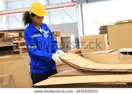 African american engineer woman wearing safety helmet and vest holding card box in the automotive part warehouse.Products and corrugated cardboard. Factory female worker in the manufacture of paper.