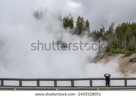 Unrecognizable tourist taking pictures of geothermal activity in Yellowstone National Park during autumn in Wyoming, USA