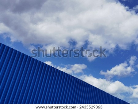 Blue metal plate against blue cloudy sky. Siding. Seamless surface of galvanized steel. Industrial building wall made of corrugated metal sheet, flat background photo texture. Royalty-Free Stock Photo #2435529863
