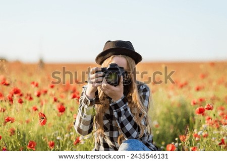 A woman wearing hat and glasses is taking picture field red flowers. Concept of serenity and beauty, as woman captures the vibrant colors flowers in her photograph