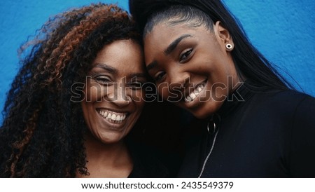 African American adolescent daughter kissing mother in the forehead showing family love and tenderness standing on blue wall. Parent and child bonding affectionate moment