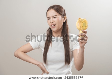 Suffering summer heat wave stroke, hot weather, tired asian young woman sweaty and thirsty, refreshing with hand in blowing, wave fan to ventilation when temperature high, isolated on background. Royalty-Free Stock Photo #2435553879