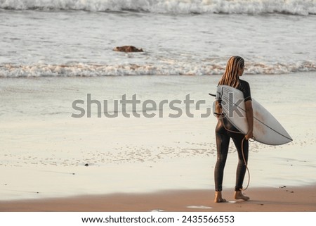 Unrecognizable young surfer woman with wetsuit and surfboard entering the sea Royalty-Free Stock Photo #2435566553