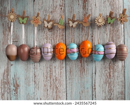 colorful Easter eggs are hung on ribbons on a jute rope with decorative clips in the form of butterflies and flowers made of natural materials on an aged wooden background.  Royalty-Free Stock Photo #2435567245