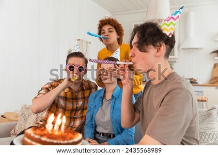 Make a wish. Woman wearing party cap blowing out burning candles on birthday cake. Happy Birthday party. Group of friends wishes girl happy birthday. People celebrating birthday with party at home