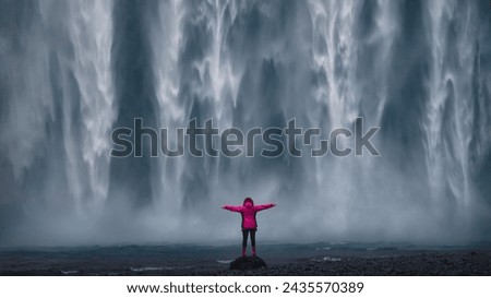 Girl awe in front of famous Iceland waterfall Skogafoss with powerfull water wall 