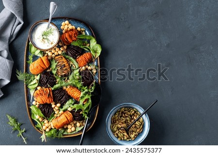 Root vegetables roast until soft in the center and crispy with chickpeas, pumpkin seeds and fresh lettuce leaves. Healthy fresh salad. Top view