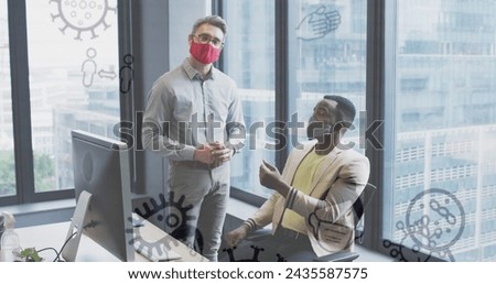 Image of virus icons over diverse businessmen with face masks talking in office. global business and digital interface during covid 19 pandemic concept digitally generated image.