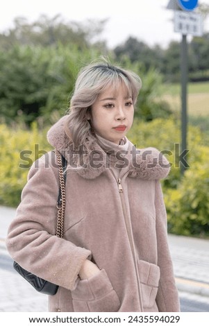 A young Chinese woman in her 20s dressed in winter walking in a park by the sea where you can see the skyscrapers of Kowloon, Hong Kong