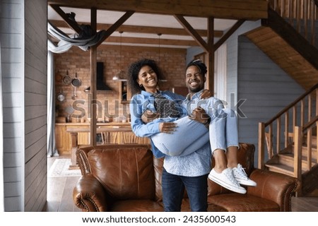 Happy African newly-weds couple arrive to own house, husband holding carry beloved smiling wife, family celebrate relocation day to their first property. Mortgage, start new independent life concept Royalty-Free Stock Photo #2435600543