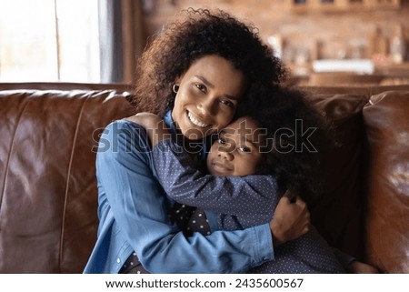 Happy Mother Day concept. Cute 6s girl cuddling loving mom smiling family sit on sofa smile looking at camera. Young woman hugging her adorable little daughter enjoy moment of tenderness feeling love Royalty-Free Stock Photo #2435600567