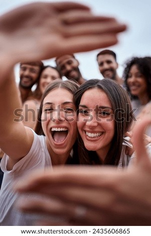 Vertical photo. Two girl friends making a frame with hands. A group of young people is happily celebrating, taking a selfie together. Smiling women having fun during their leisure travel