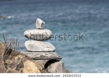 Inukshuk, is a stack of various sized rocks in the shape of a person. The formation is a symbol of direction. The Inuit traditional figure is high on a hill. The background is a blue ocean.