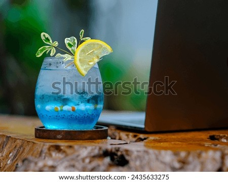 A fresh and cold blue drink mixed with small round jelly and garnished with sliced lemon is served on an aesthetic wooden table. Royalty-Free Stock Photo #2435633275