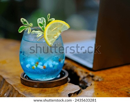 A fresh and cold blue drink mixed with small round jelly and garnished with sliced lemon is served on an aesthetic wooden table. Royalty-Free Stock Photo #2435633281