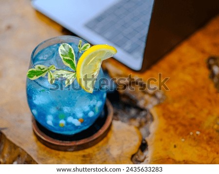 A fresh and cold blue drink mixed with small round jelly and garnished with sliced lemon is served on an aesthetic wooden table. Royalty-Free Stock Photo #2435633283