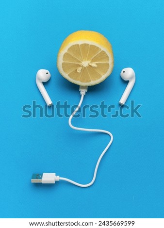 Half a lemon with wireless headphones and USB cable on a blue background. The concept of listening to music tracks. Royalty-Free Stock Photo #2435669599
