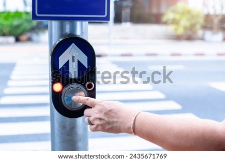 Close up pedestrian crossing call button. Hand pushing button to cross. The push button on the light pole is used when crossing a zebra crossing.