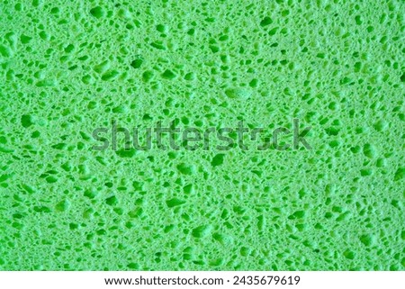 Green sponge with pores texture background for graphics. Close-up macro photo of household sponge tissue.