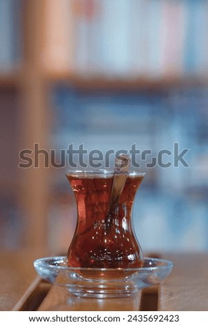 Traditional Turkish tea served in a thin belly glass, set against a blurred background of bookshelves in a library.