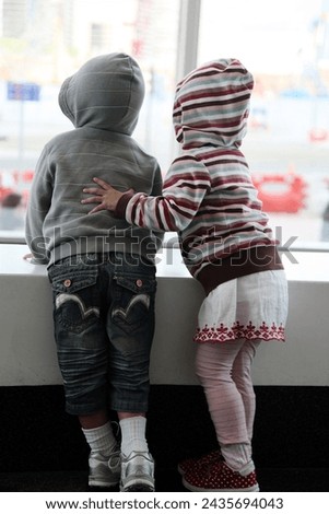 Exterior photo visual of 2 young friends kids childs children boy and girl view from th back taking care of each other looking at or watching something out of frame for curiosity observing curious 