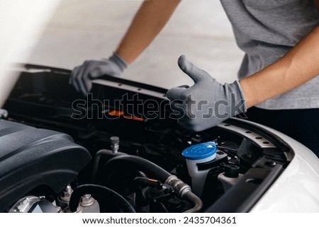 Hand of client showing thumb up for approval of car repair work, Mechanic working under the hood of car.
