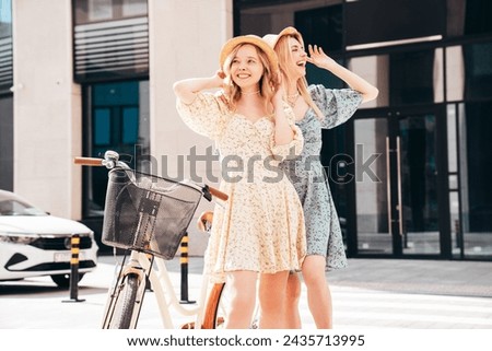 Two young beautiful smiling hipster woman in trendy summer sundress. Carefree women riding retro bicycle. Positive models having fun on bike posing in the park in hats. Best friends outdoors Royalty-Free Stock Photo #2435713995