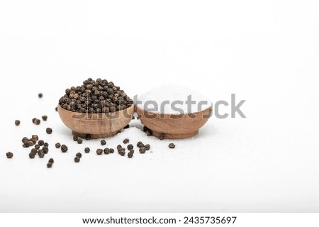 Isolated black peppercorns next to fine grain table salt