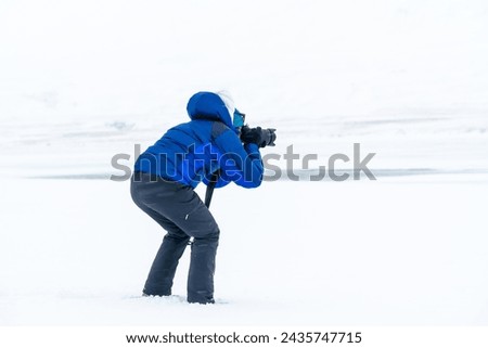 Adventurous photographer woman in winter in Iceland photographing on a frozen lake below zero