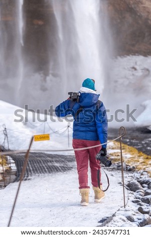 Female photographer from behind in winter in Iceland visiting the Seljalandsfoss waterfall