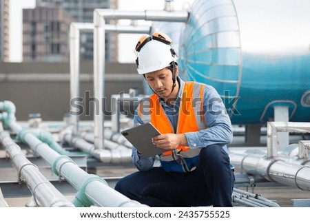 Asian male engineer working at construction site area. Male engineer worker standing near sewer pipes or water tank area. Asian male plumber worker maintenance sewer pipes network system Royalty-Free Stock Photo #2435755525